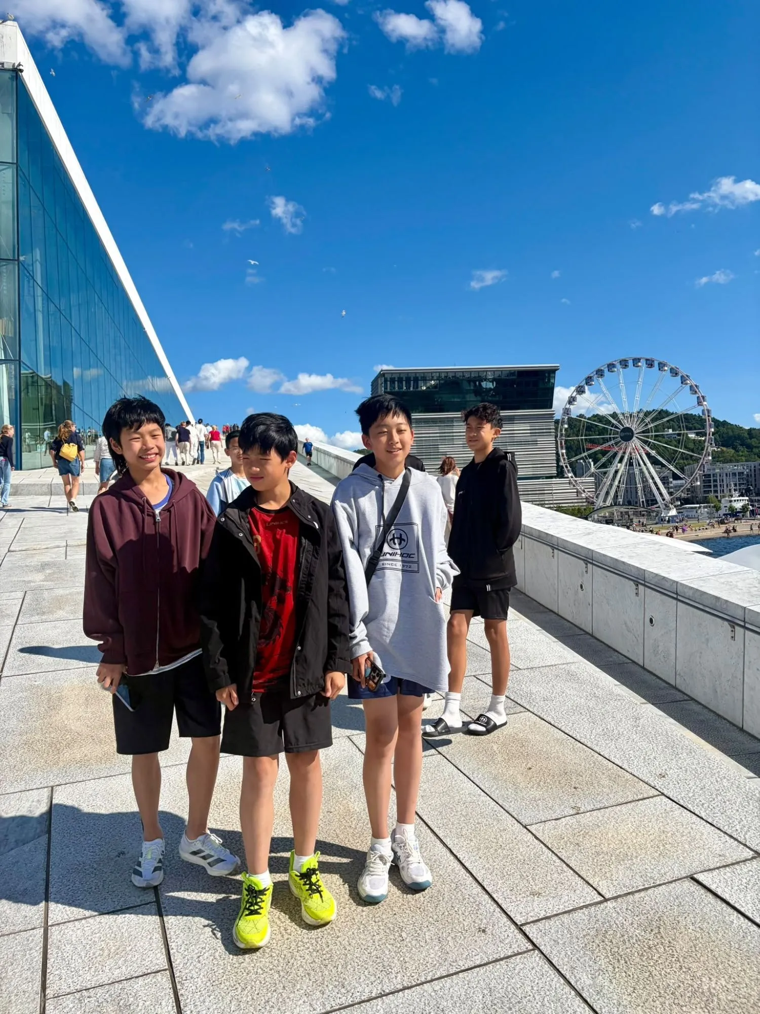 Four boys smiling on the roof of the Oslo Opera House with a Ferris wheel behind them