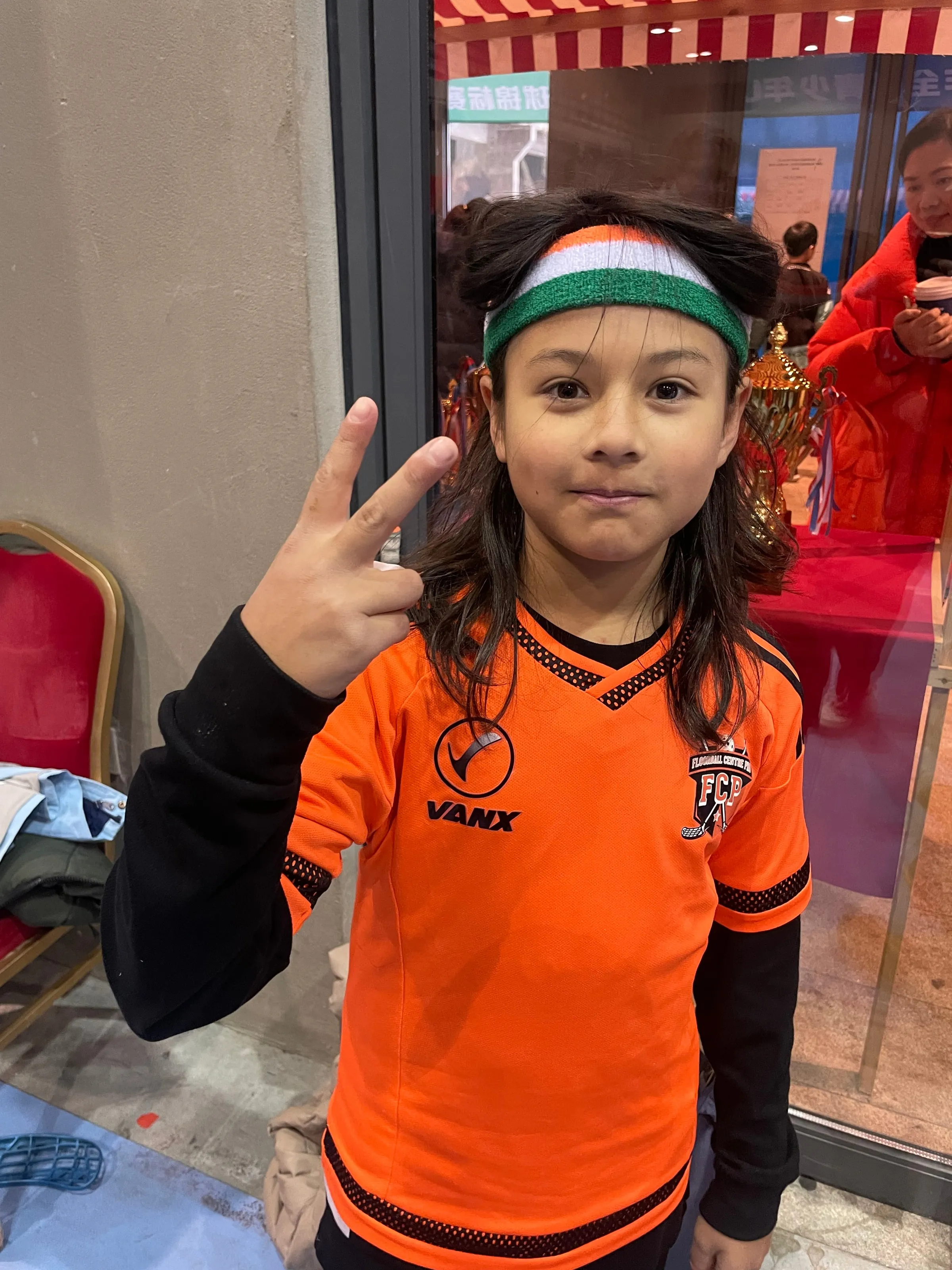 Smiling girl in an orange jersey and headband making a peace sign