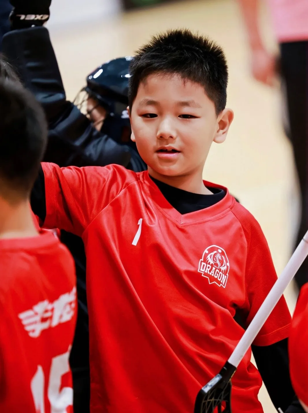 Boy in a red jersey holding a floorball stick