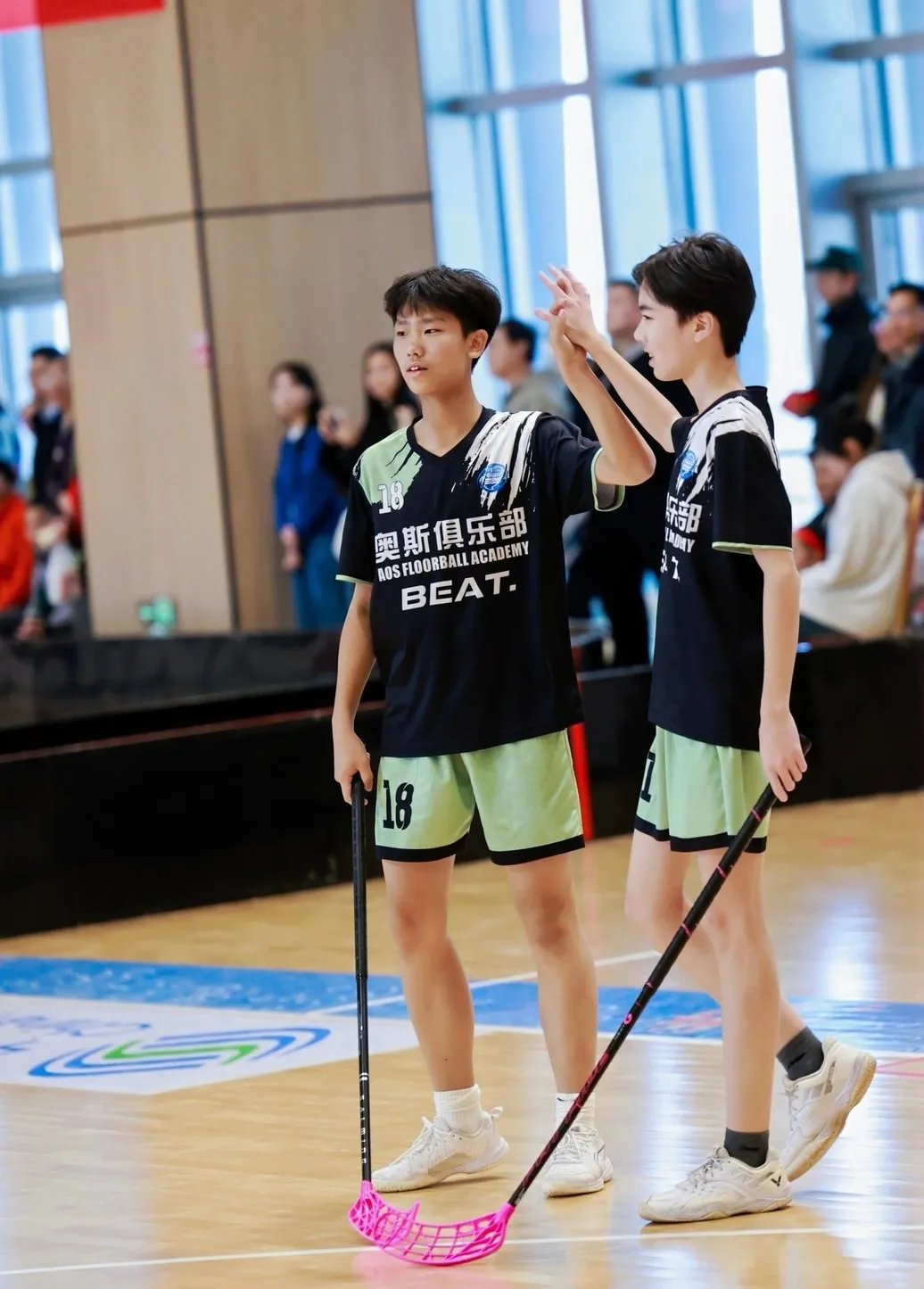 Two players walking across the court with floorball sticks